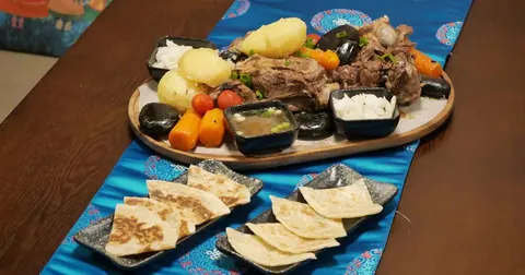 木盘上的石烤羊肉 Khorkhog，配土豆、胡萝卜和烤饼