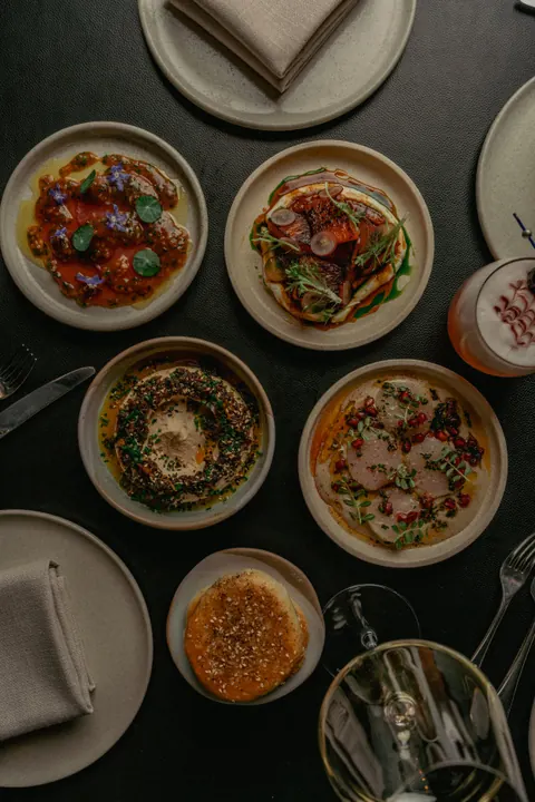 Maha 官网餐桌照片，展示鹰嘴豆泥、蔬菜、面包及多款小盘菜